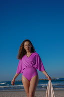 A woman wearing a pink one-piece swimsuit with a skirt standing on a beach